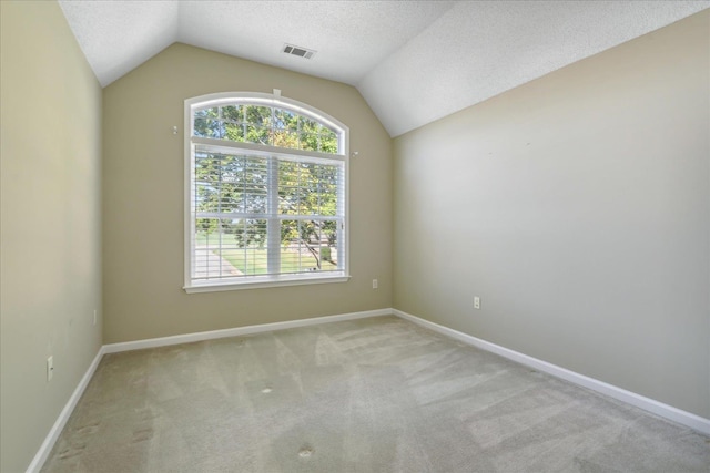 carpeted spare room with a textured ceiling and vaulted ceiling