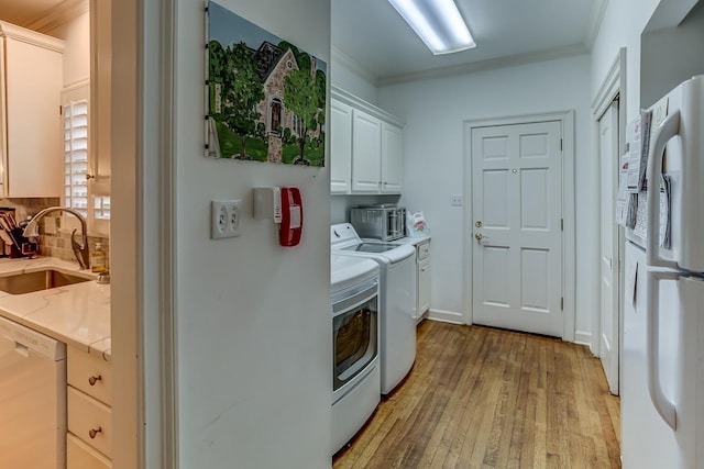 laundry area with crown molding, light wood-type flooring, independent washer and dryer, and sink