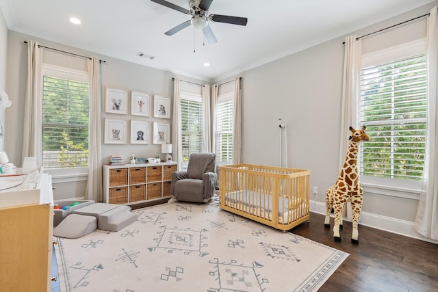 bedroom with hardwood / wood-style floors, a crib, and multiple windows