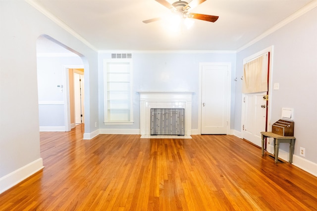 unfurnished living room with built in shelves, ceiling fan, light hardwood / wood-style flooring, and ornamental molding