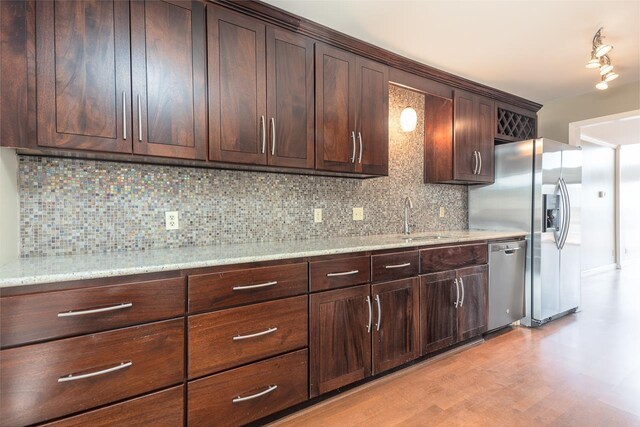 kitchen with sink, stainless steel appliances, dark brown cabinetry, tasteful backsplash, and light stone countertops