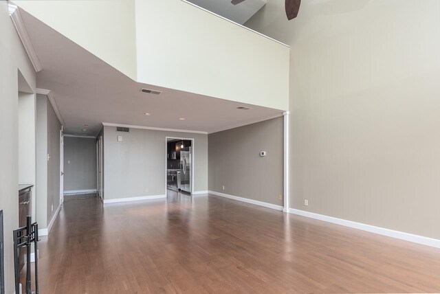 unfurnished living room featuring wood-type flooring, ornamental molding, ceiling fan, and a towering ceiling