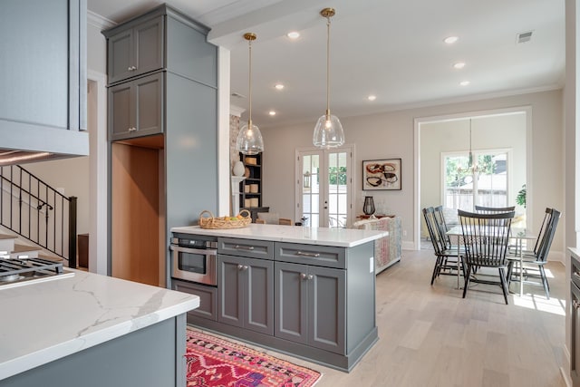 kitchen featuring gray cabinetry, light stone counters, decorative light fixtures, appliances with stainless steel finishes, and light wood-type flooring