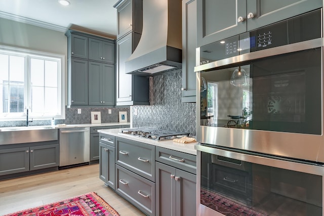 kitchen with custom range hood, stainless steel appliances, a healthy amount of sunlight, and sink