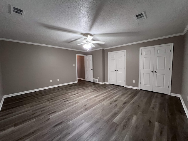 unfurnished bedroom featuring dark wood-type flooring, ceiling fan, ornamental molding, a textured ceiling, and multiple closets