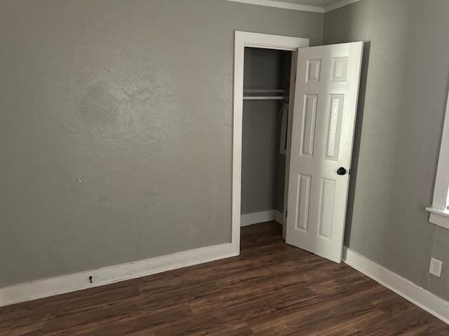 unfurnished bedroom with a closet, crown molding, and dark wood-type flooring