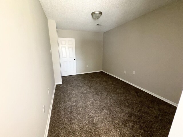 unfurnished room with dark colored carpet and a textured ceiling