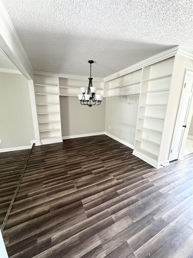 unfurnished dining area featuring built in shelves, a textured ceiling, dark wood-type flooring, crown molding, and an inviting chandelier