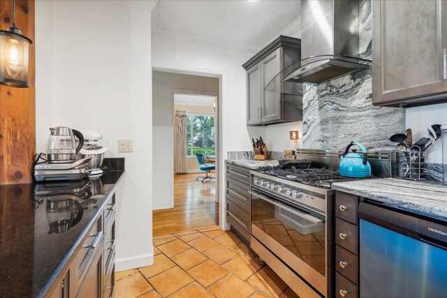 kitchen featuring appliances with stainless steel finishes, wall chimney range hood, dark stone counters, and light tile flooring