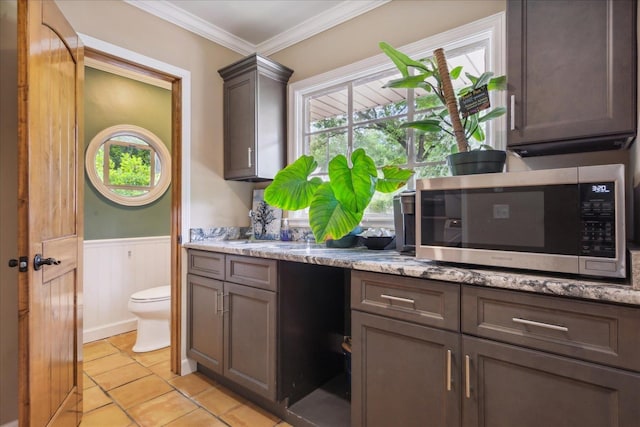 kitchen with dark brown cabinetry, light stone countertops, light tile flooring, and crown molding