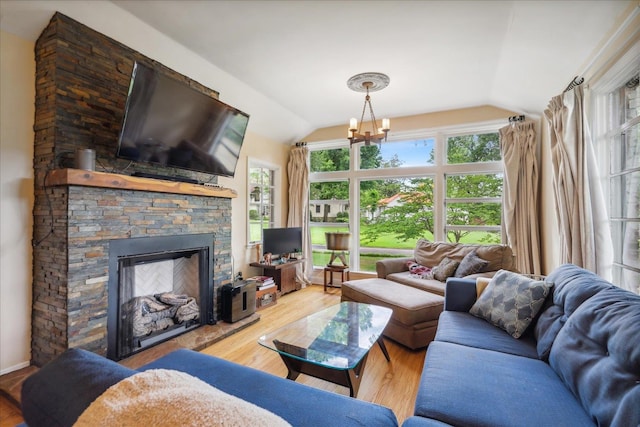 living room featuring a stone fireplace, hardwood / wood-style flooring, vaulted ceiling, and an inviting chandelier