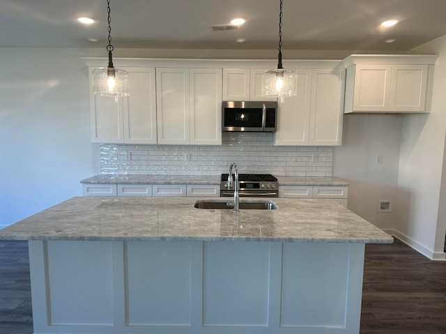 kitchen featuring pendant lighting, stainless steel microwave, an island with sink, and white cabinetry