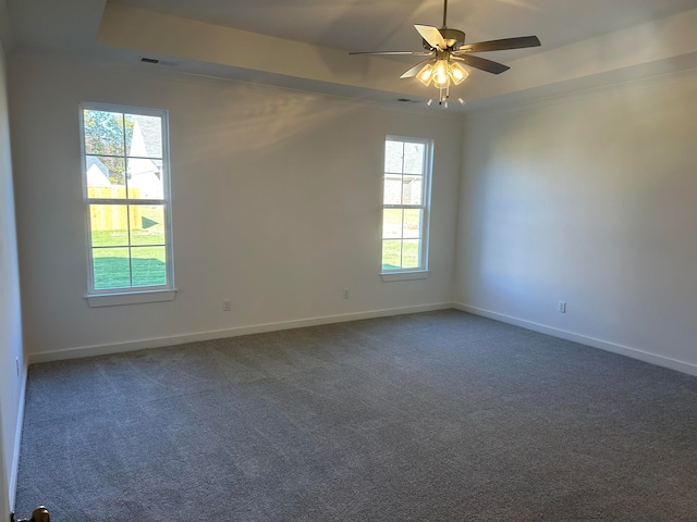 unfurnished room featuring dark carpet, a tray ceiling, plenty of natural light, and ceiling fan