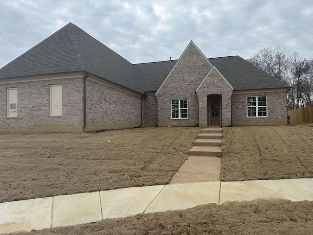 french provincial home with brick siding and a shingled roof