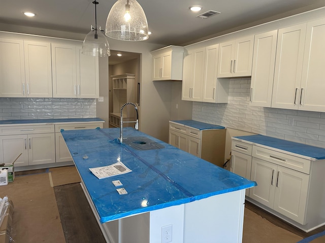 kitchen with white cabinetry, backsplash, decorative light fixtures, and a center island with sink