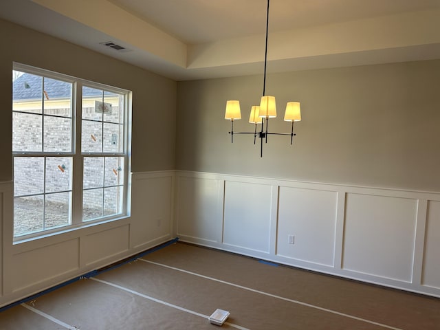 unfurnished dining area featuring a chandelier, visible vents, a wainscoted wall, and a decorative wall