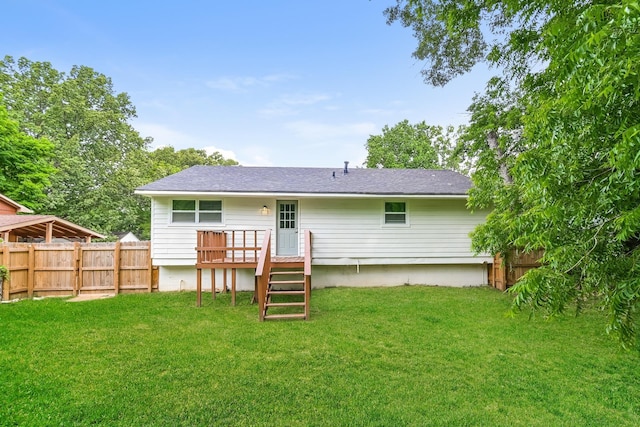 rear view of property with a fenced backyard, a wooden deck, a lawn, and roof with shingles