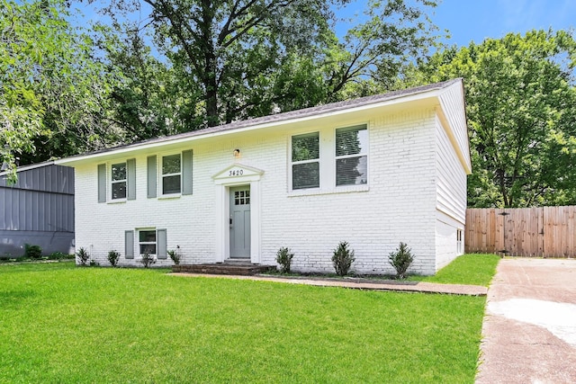 raised ranch featuring brick siding, fence, and a front yard