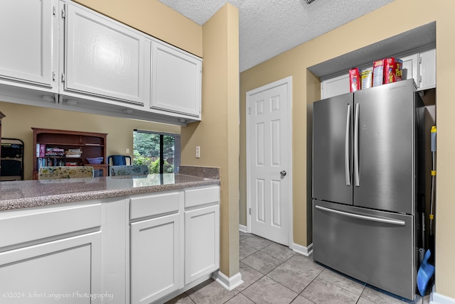 kitchen featuring a textured ceiling, light tile patterned floors, white cabinetry, and stainless steel refrigerator