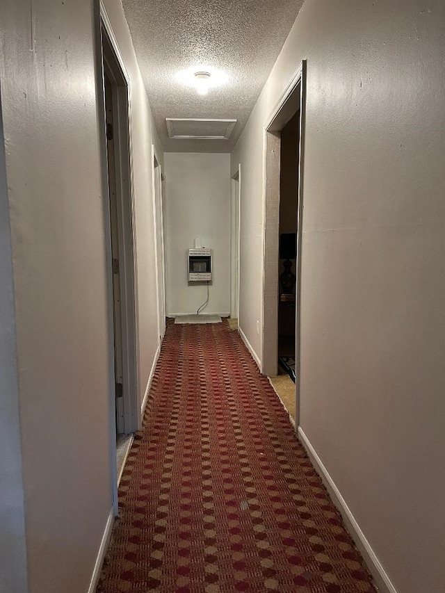 hall featuring heating unit, carpet, baseboards, attic access, and a textured ceiling