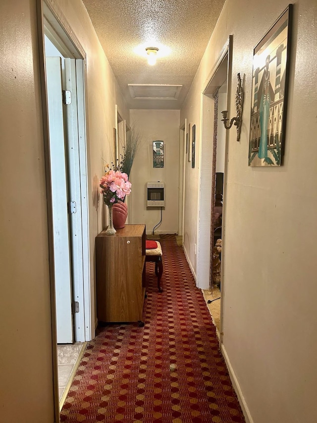 hallway with heating unit, carpet flooring, a textured ceiling, and attic access