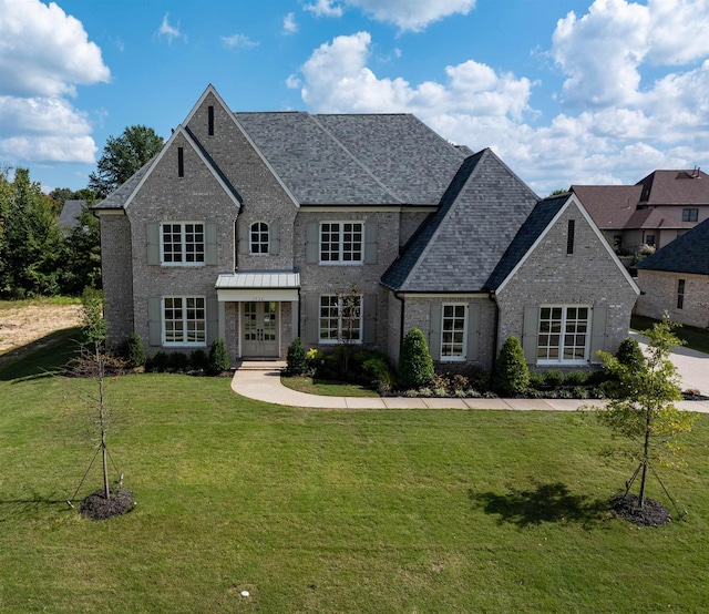 french country style house featuring brick siding, french doors, a front lawn, and roof with shingles