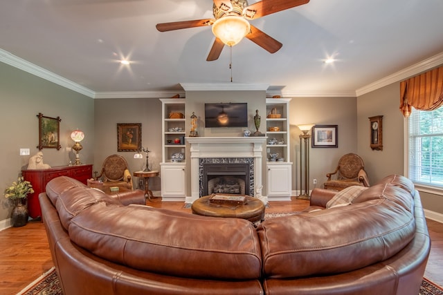 living room featuring ceiling fan, built in features, light wood-type flooring, a fireplace, and ornamental molding