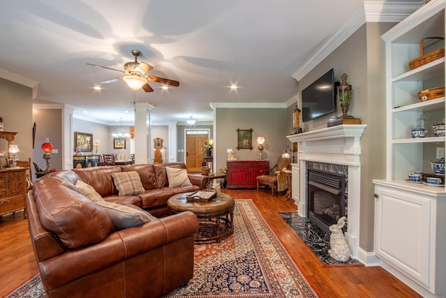 living room featuring ceiling fan with notable chandelier, crown molding, hardwood / wood-style flooring, built in features, and a premium fireplace