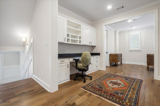 home office featuring dark wood-type flooring, ornamental molding, and built in desk