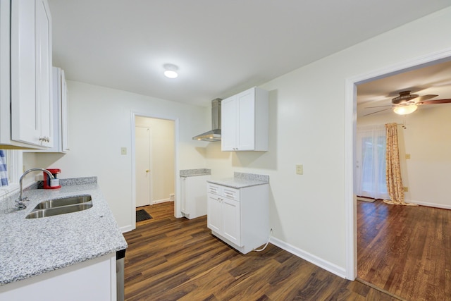 kitchen with dark wood-type flooring, white cabinetry, a sink, wall chimney range hood, and light stone countertops