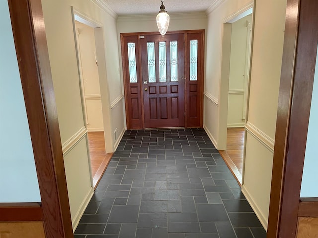 entryway with a textured ceiling, ornamental molding, and dark tile flooring