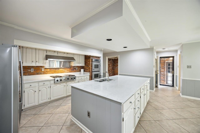 kitchen with appliances with stainless steel finishes, a kitchen island with sink, range hood, light tile patterned flooring, and decorative backsplash