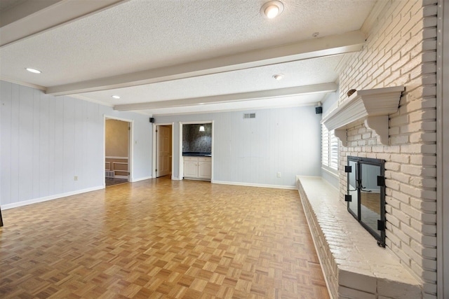 unfurnished living room with a fireplace, light parquet flooring, beam ceiling, and a textured ceiling