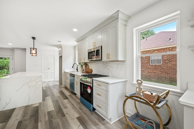 kitchen with hanging light fixtures, appliances with stainless steel finishes, a wealth of natural light, and white cabinets