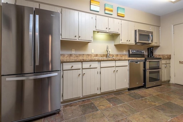 kitchen with sink, dark tile patterned flooring, stainless steel appliances, and white cabinetry