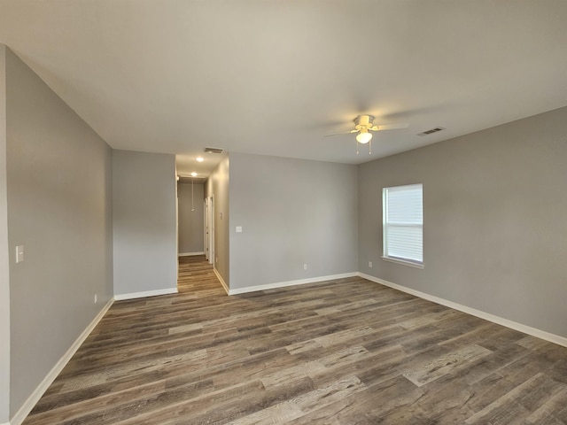 empty room featuring a ceiling fan, baseboards, visible vents, and dark wood-style flooring