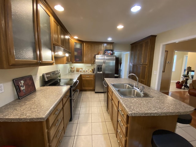 kitchen featuring light tile patterned flooring, sink, stainless steel appliances, and an island with sink