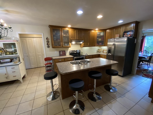 kitchen with a breakfast bar, appliances with stainless steel finishes, light tile patterned floors, and a kitchen island with sink