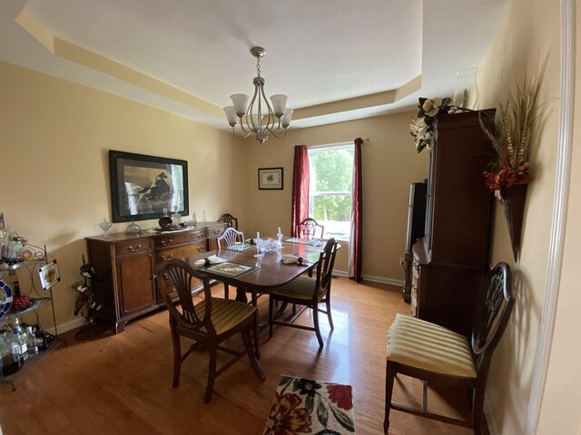 dining space with a chandelier, light wood-type flooring, and a raised ceiling