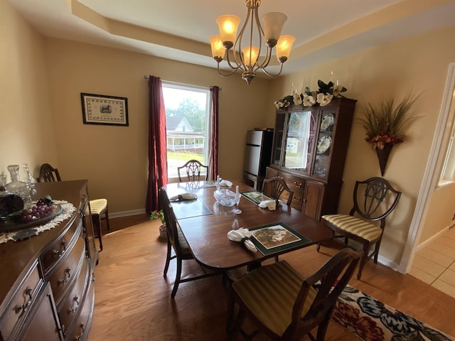 dining room featuring a raised ceiling, light hardwood / wood-style floors, and an inviting chandelier