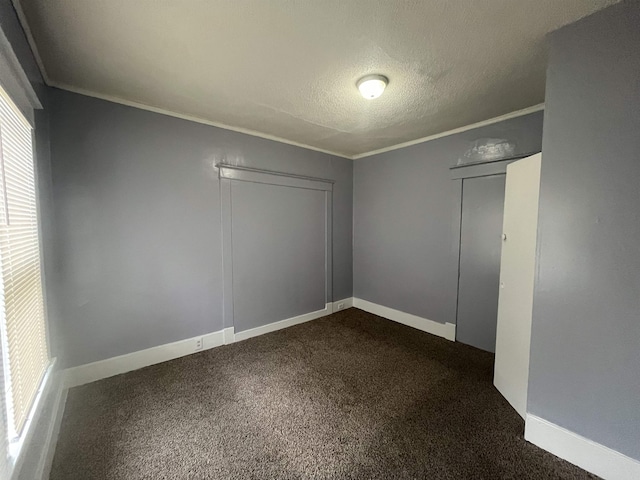 spare room with dark colored carpet, crown molding, a textured ceiling, and baseboards