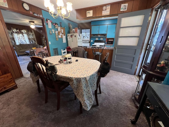 carpeted dining room featuring ceiling fan with notable chandelier and wood walls