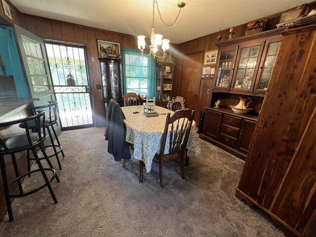 carpeted dining room featuring a chandelier, wooden walls, and a textured ceiling