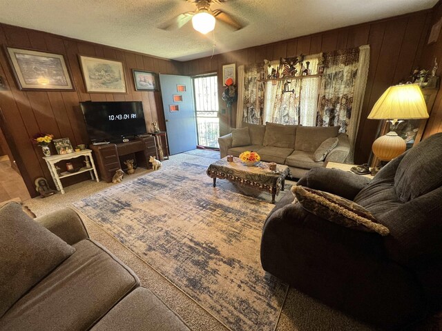 living room featuring ceiling fan, carpet, wood walls, and a textured ceiling