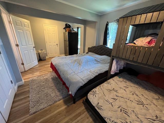 bedroom featuring hardwood / wood-style flooring, ornamental molding, and fridge