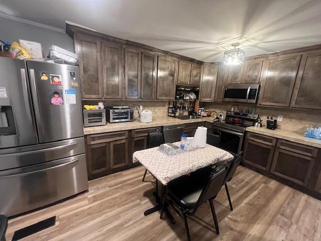 kitchen with appliances with stainless steel finishes, backsplash, dark brown cabinetry, crown molding, and light hardwood / wood-style flooring