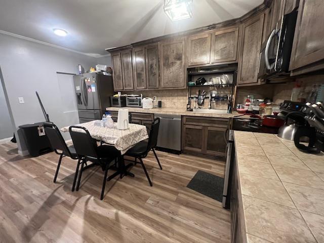 kitchen with crown molding, dark brown cabinets, tile counters, and appliances with stainless steel finishes