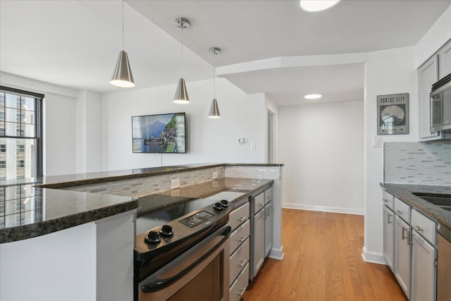 kitchen with gray cabinetry, hanging light fixtures, backsplash, dark stone countertops, and light wood-type flooring