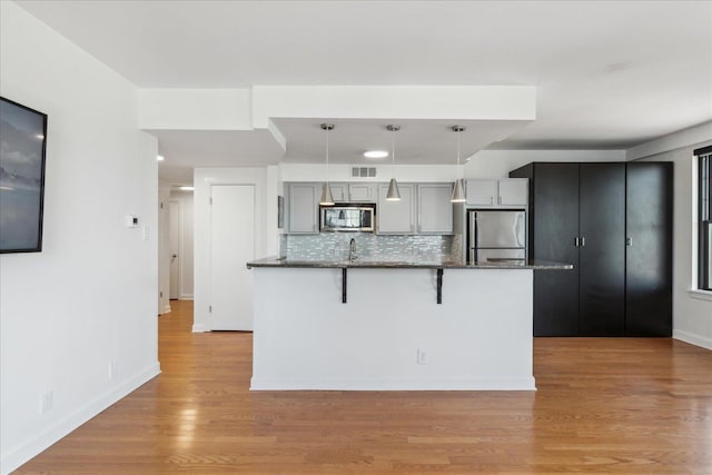 kitchen featuring gray cabinetry, tasteful backsplash, pendant lighting, appliances with stainless steel finishes, and light wood-type flooring