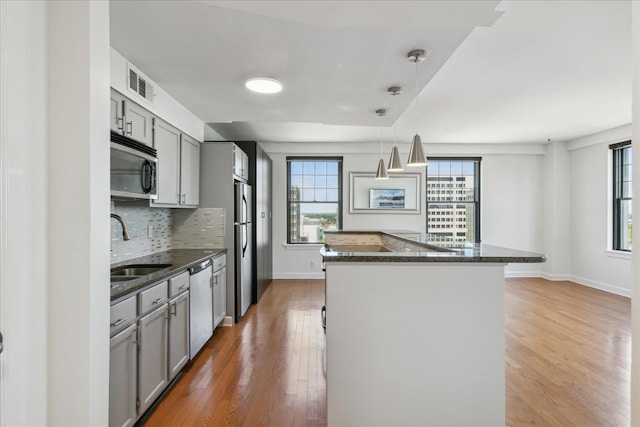 kitchen with hanging light fixtures, backsplash, hardwood / wood-style floors, gray cabinets, and appliances with stainless steel finishes